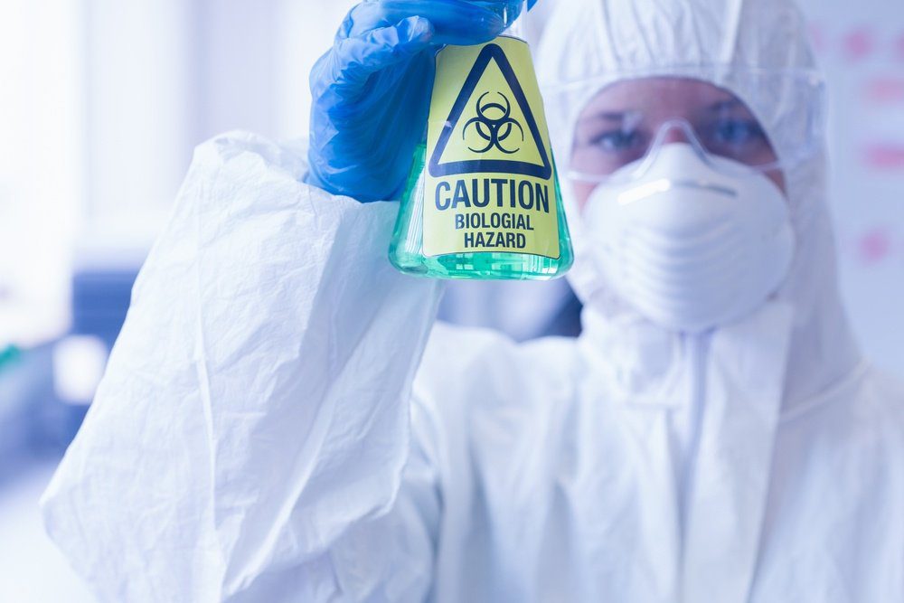 Close-up of a scientist in protective suit with hazardous blue chemical in flask at the laboratory