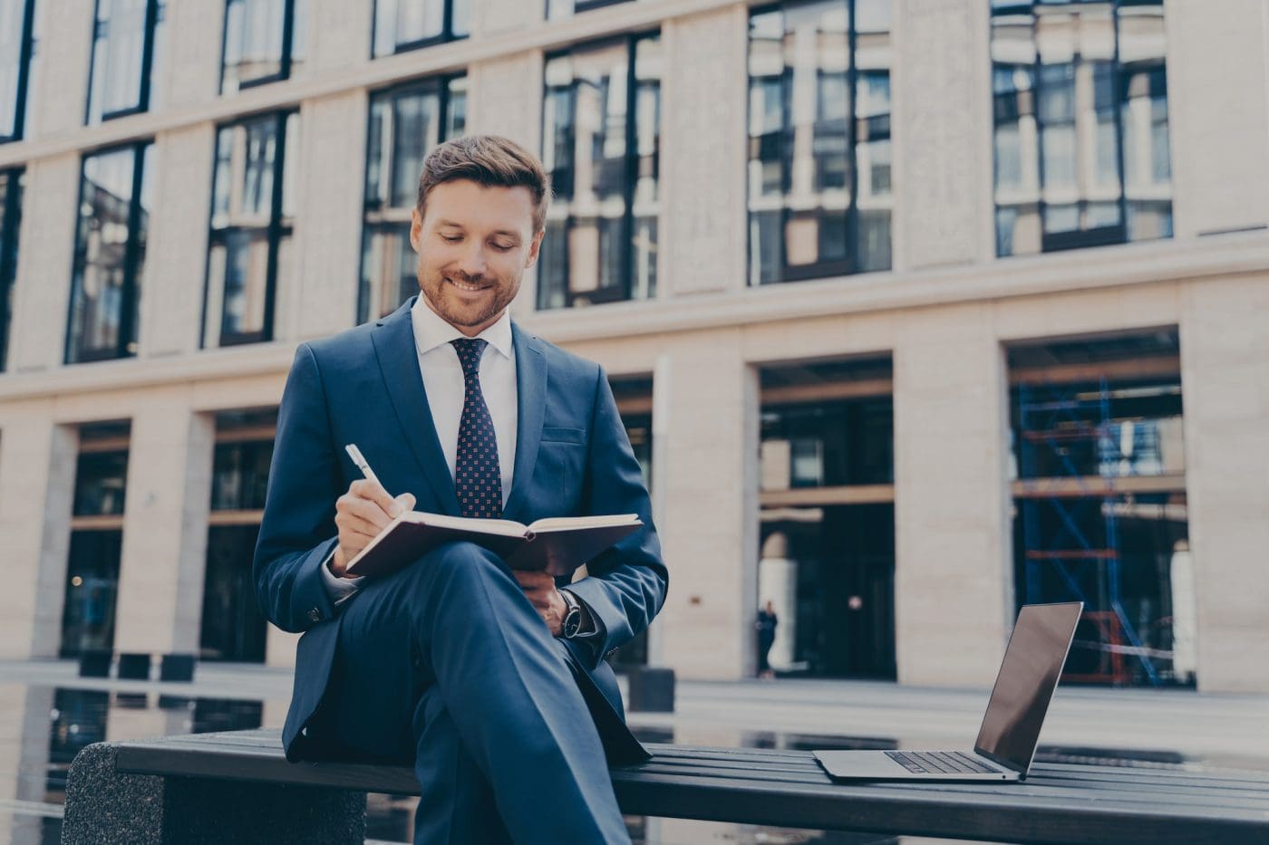 Professional office worker writing down ideas in notebook while working online outdoors