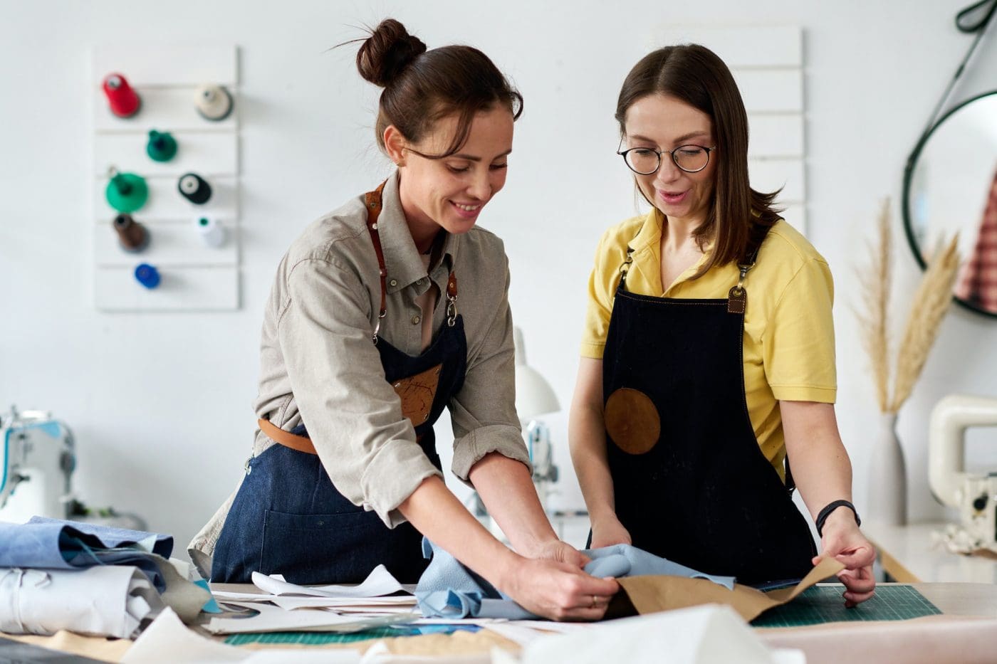 Two female tanners choosing piece of leather for sewing new apparel